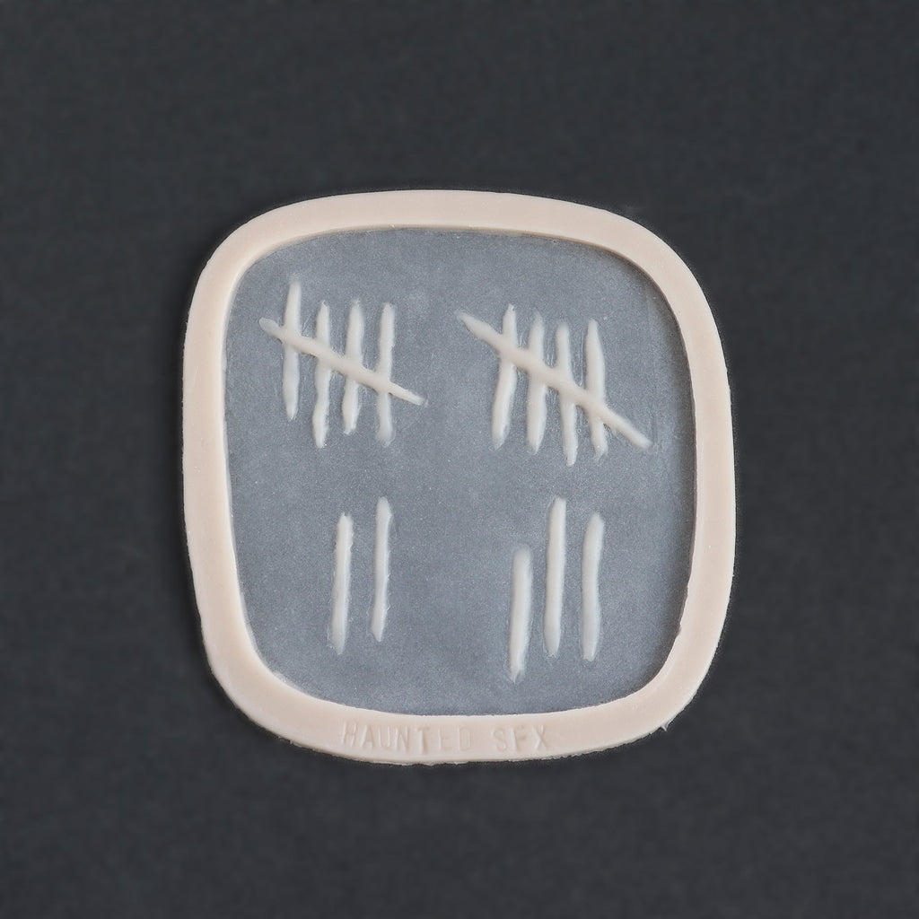 Tally Marks - Silicone makeup prosthetic in vanilla shade on a black surface