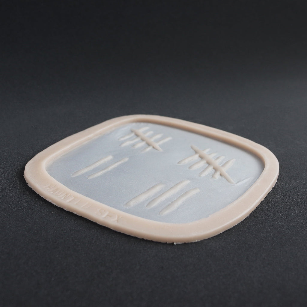 Tally Marks - Silicone makeup prosthetic in vanilla shade on a black surface