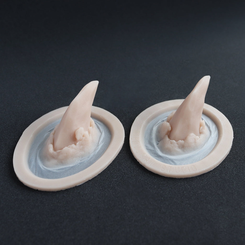 Torn Horns (Pair) - Silicone makeup prosthetic in vanilla shade on a black surface