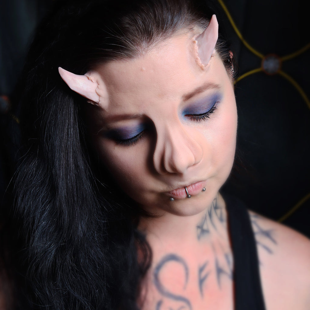 Woman with black hair wearing torn horns and a whelk nose prosthetic